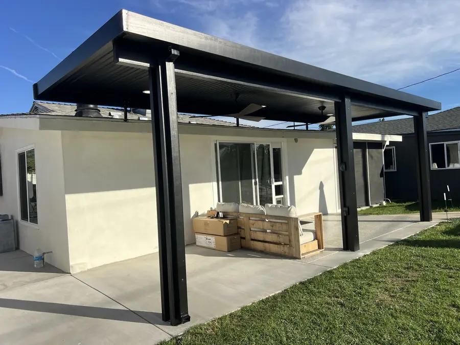 Black aluminum patio covers attached to a white stucco home in Palm Springs, CA, with ceiling fans over a concrete patio